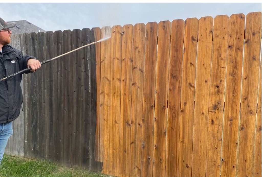 A Pro Wash technician pressure washing a weathered wooden fence